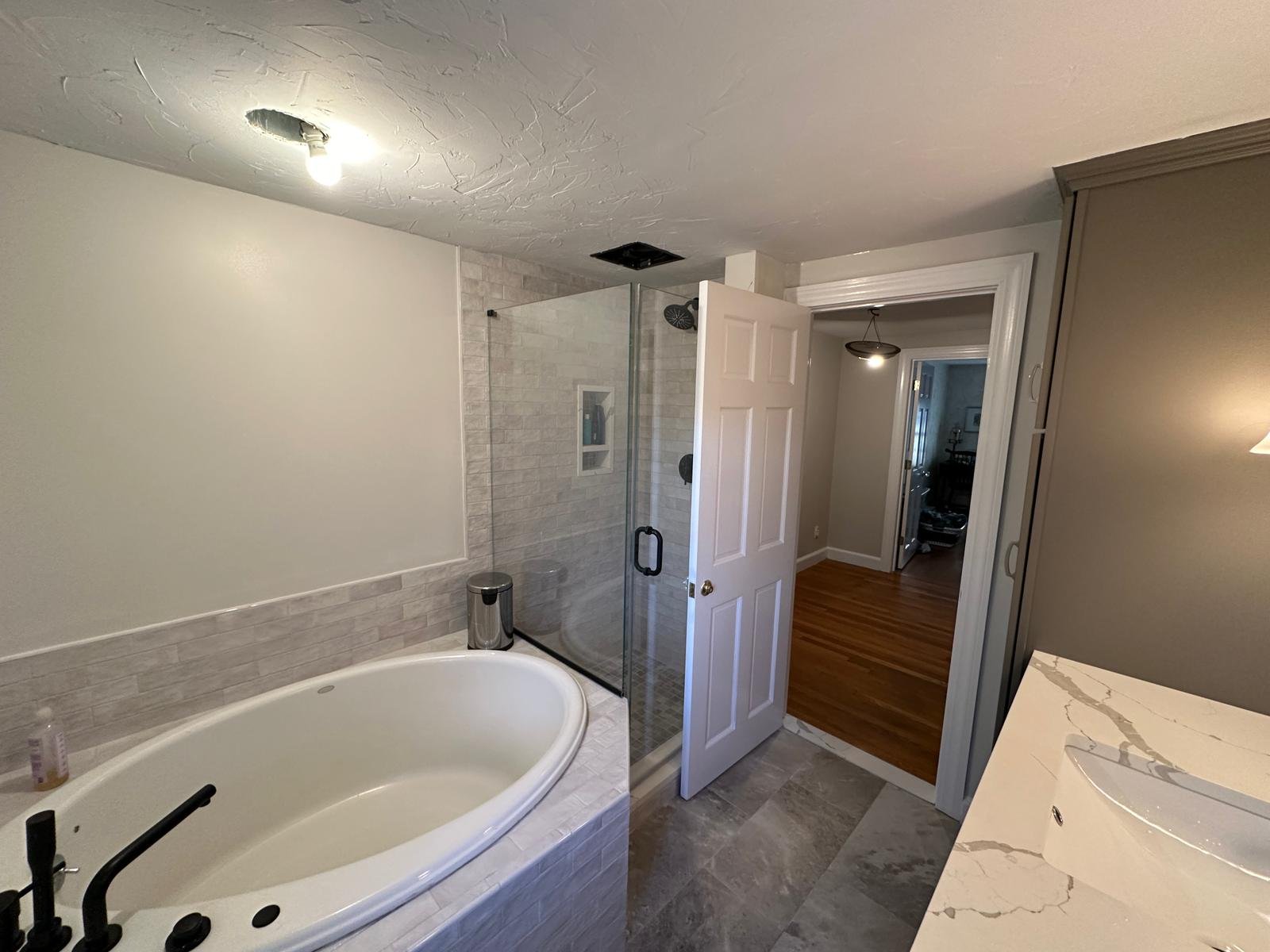 Glass shower enclosure and tiled soaking tub in a remodelled bathroom with a new door and casing