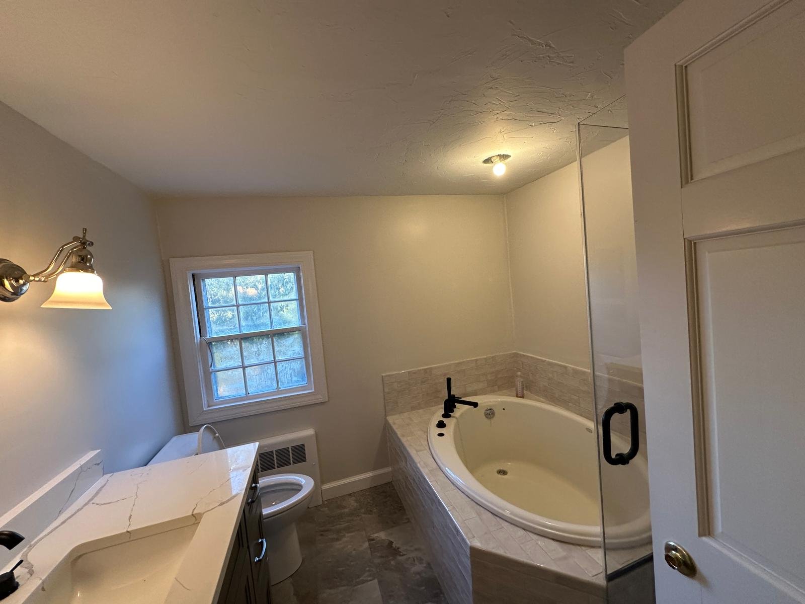 Remodelled bathroom with a quartz vanity top, sconce lighting and a tiled soaking tub by the window