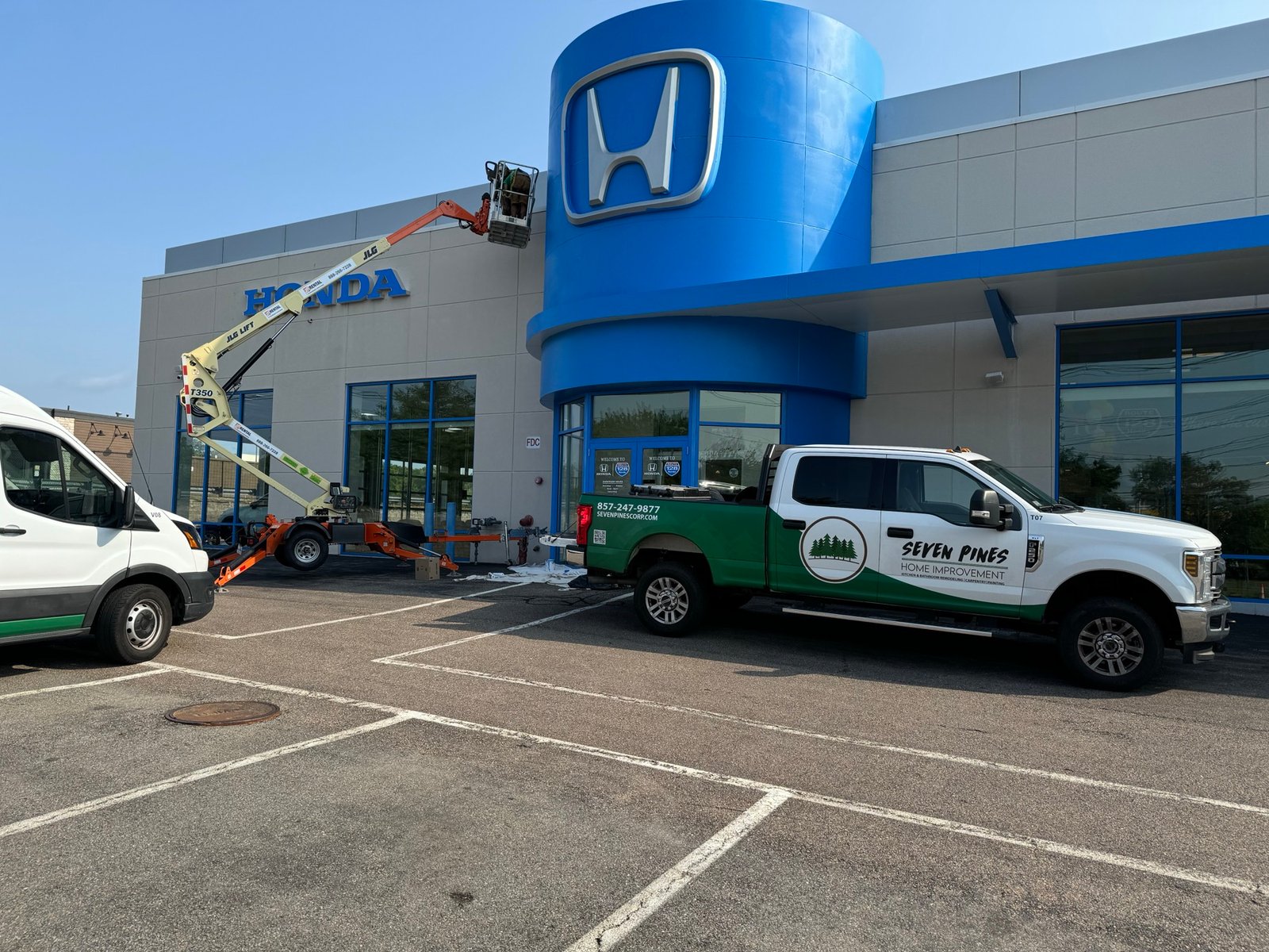 Boom lift and Seven Pines truck set up for exterior painting at a car dealership