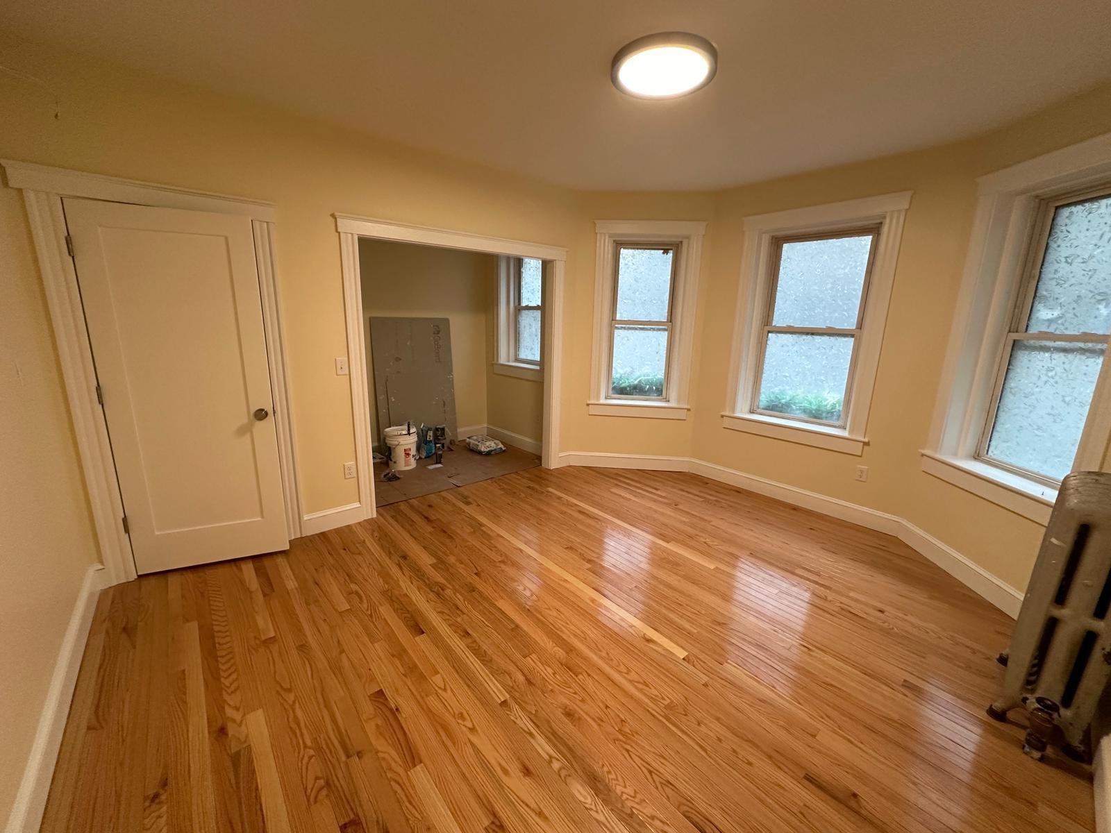 Empty renovated room with refinished hardwood floors, trimmed windows and painted walls