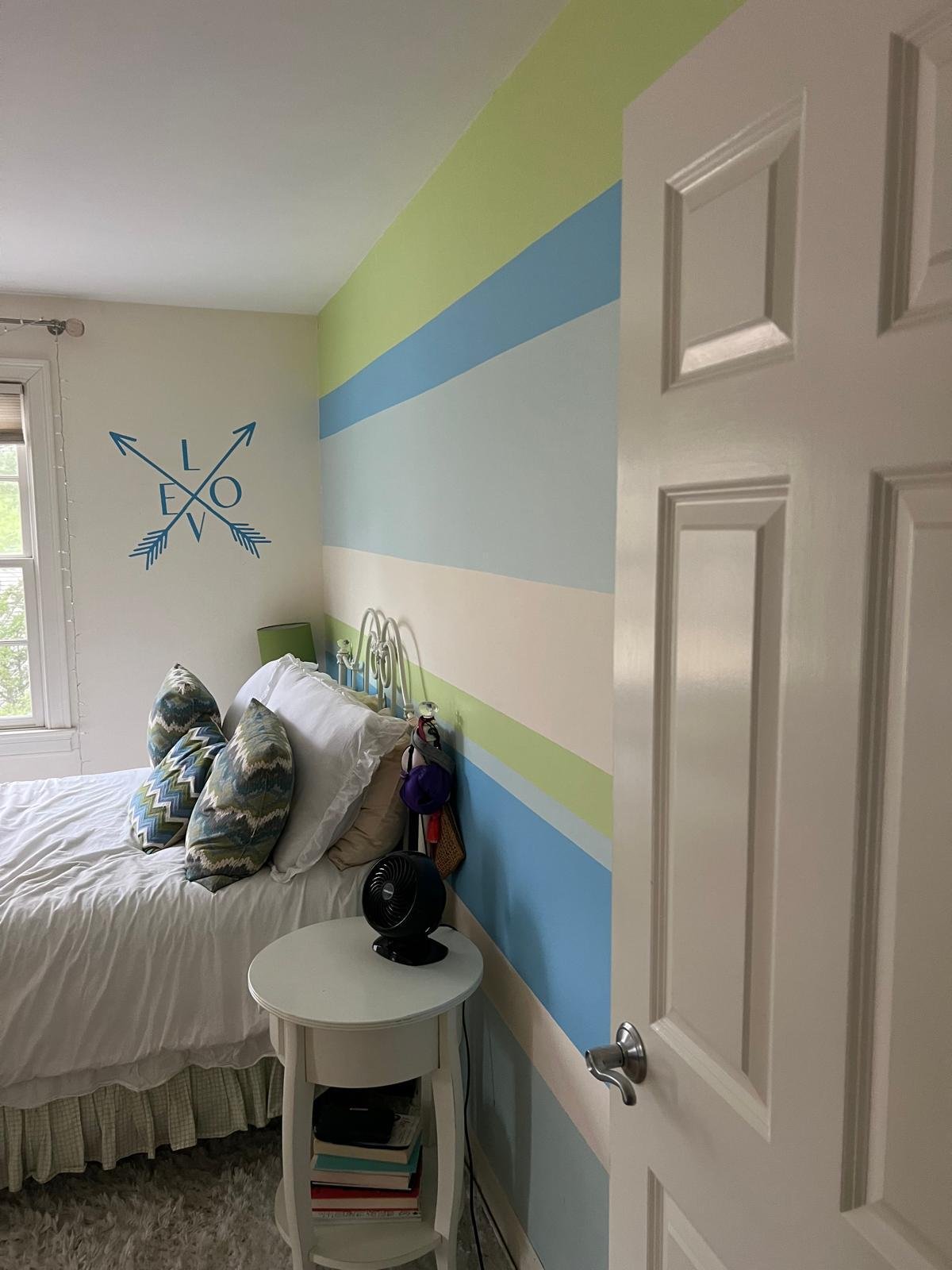 Bedroom with a painted green, blue and cream striped accent wall and white trim