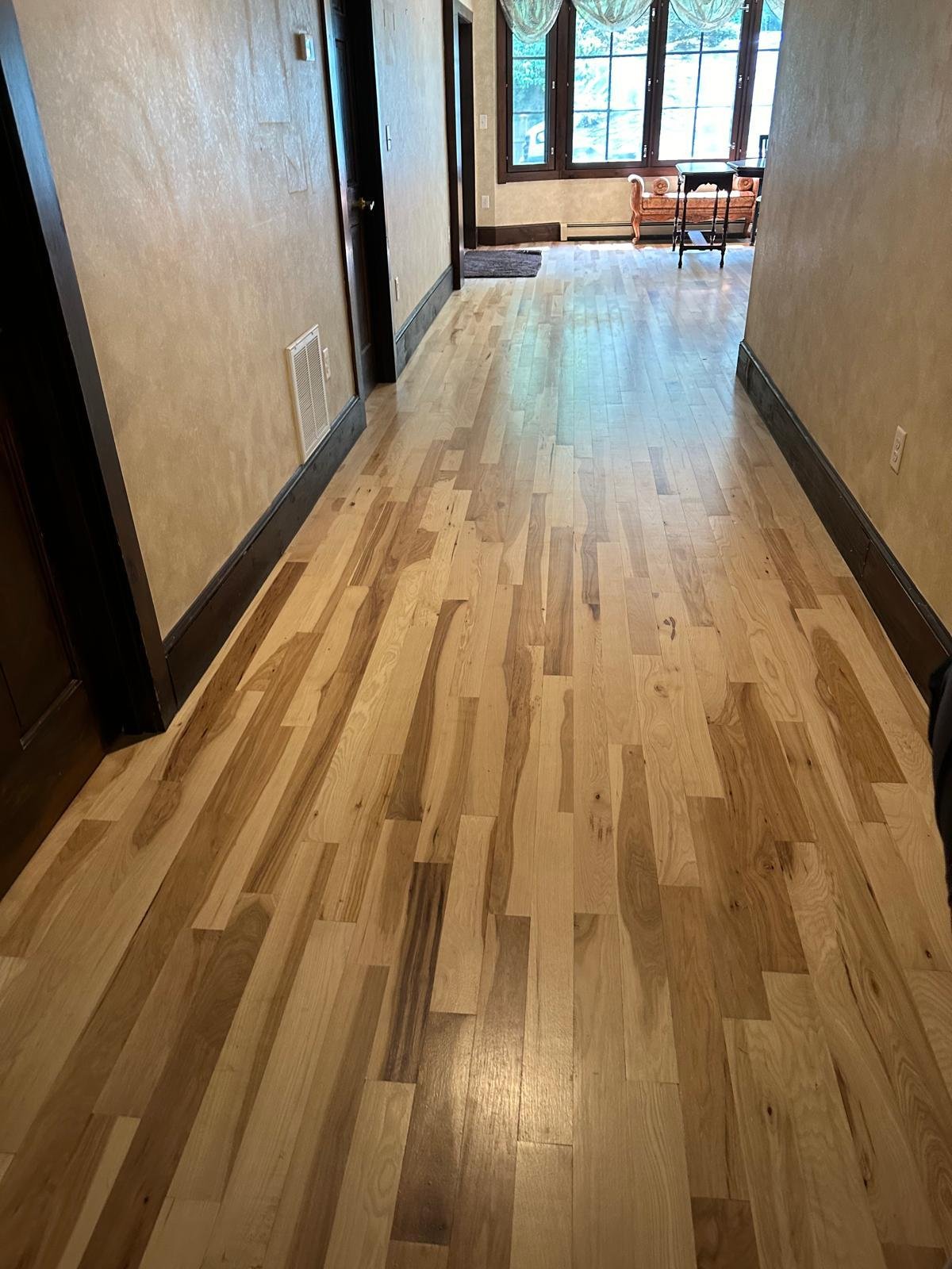 Wide maple hardwood flooring running down a hallway with dark stained baseboards