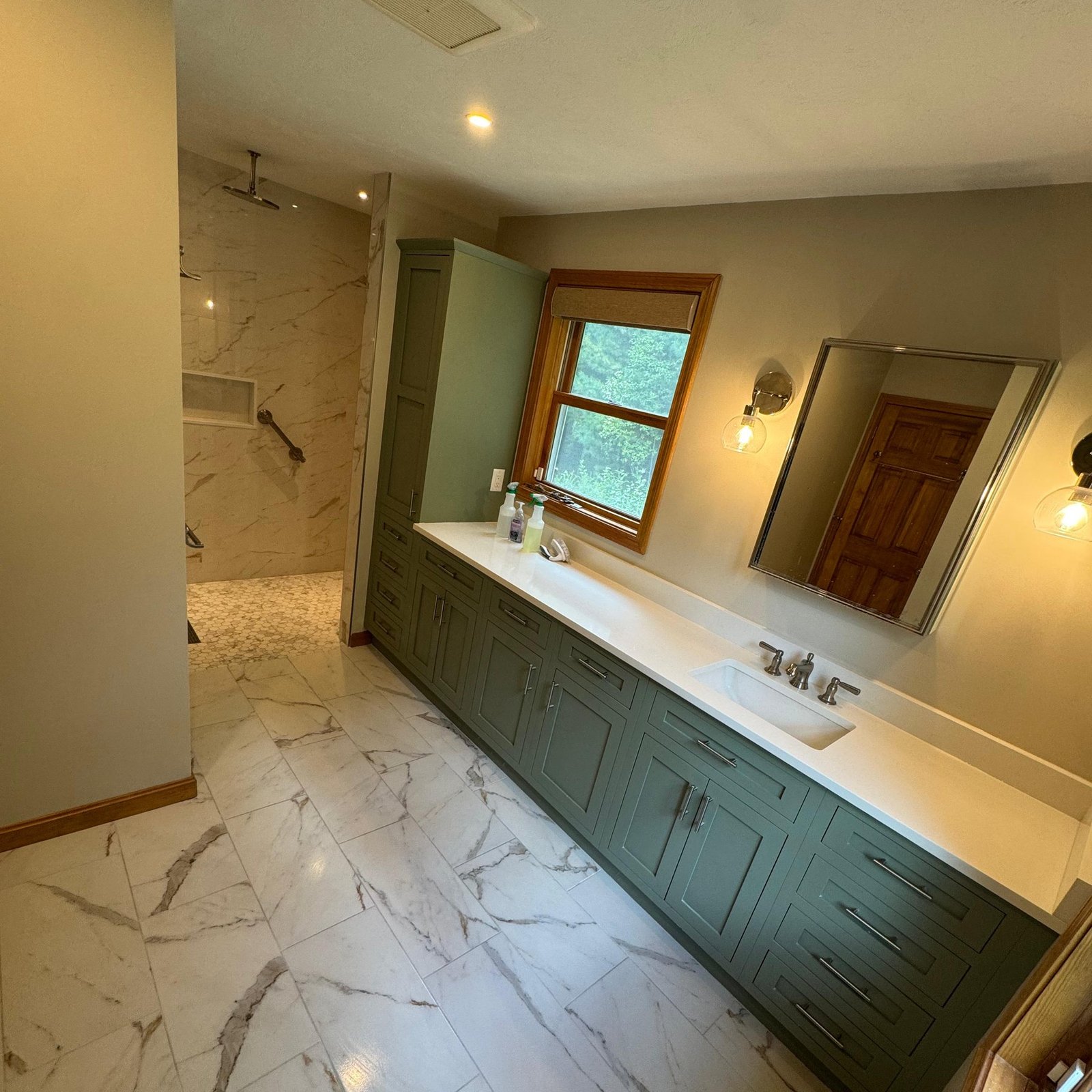 Remodeled master bathroom with a green shaker vanity, a quartz counter and marble-look porcelain tile, with a walk-in shower beyond