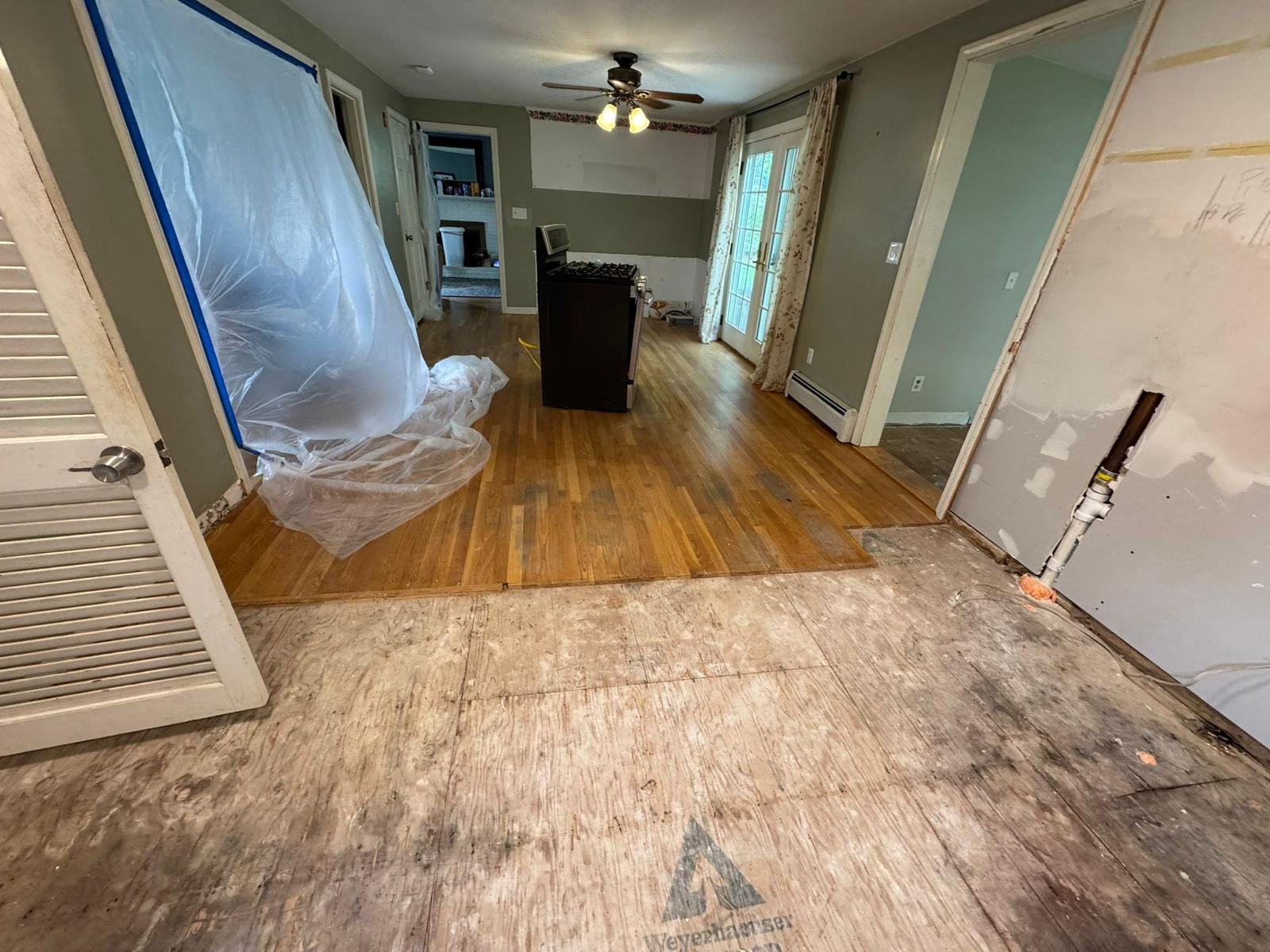 Room mid-renovation with plywood subfloor, partial hardwood and exposed drywall