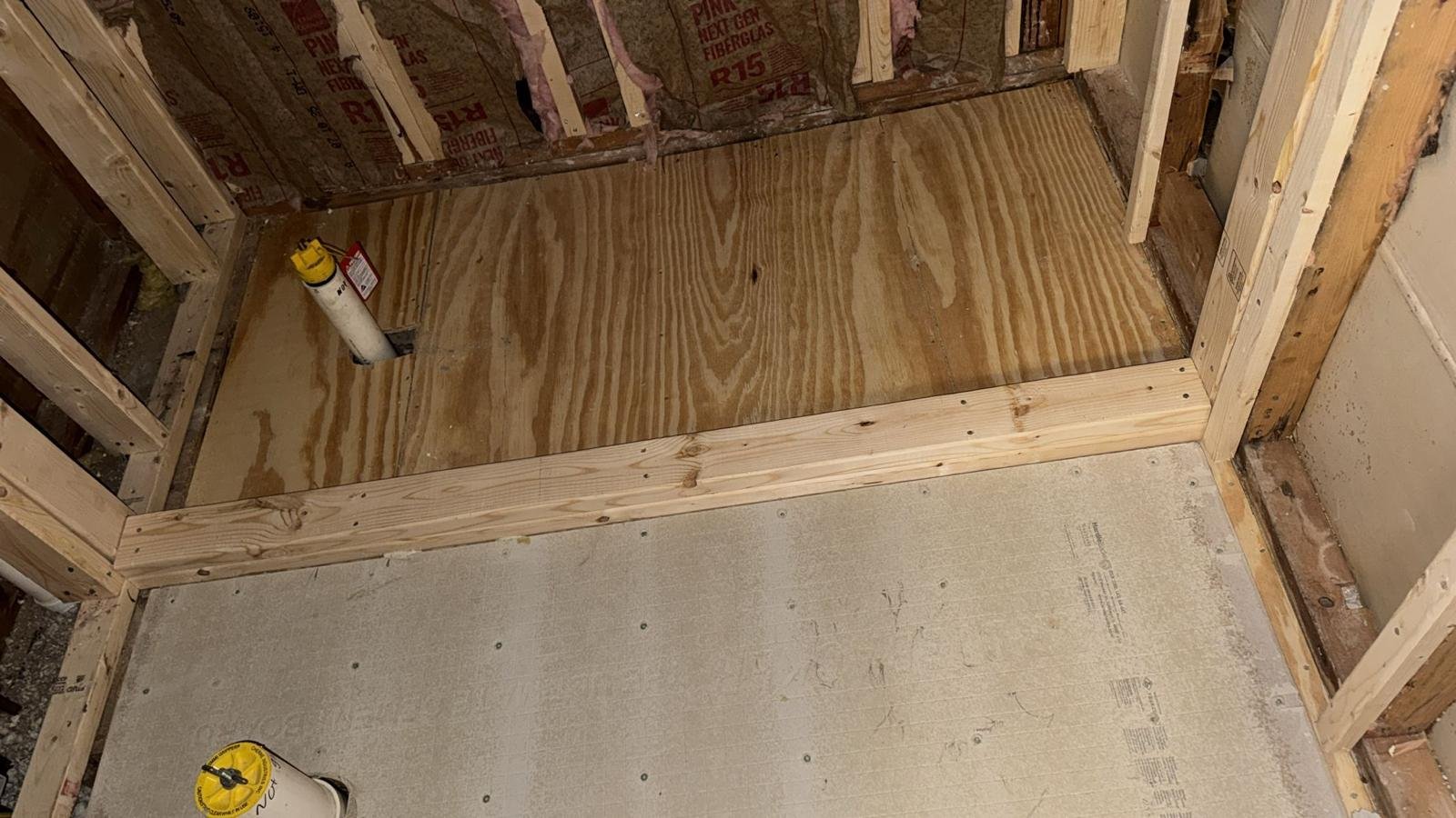 Plywood subfloor installed within new wood stud framing, with construction tools nearby
