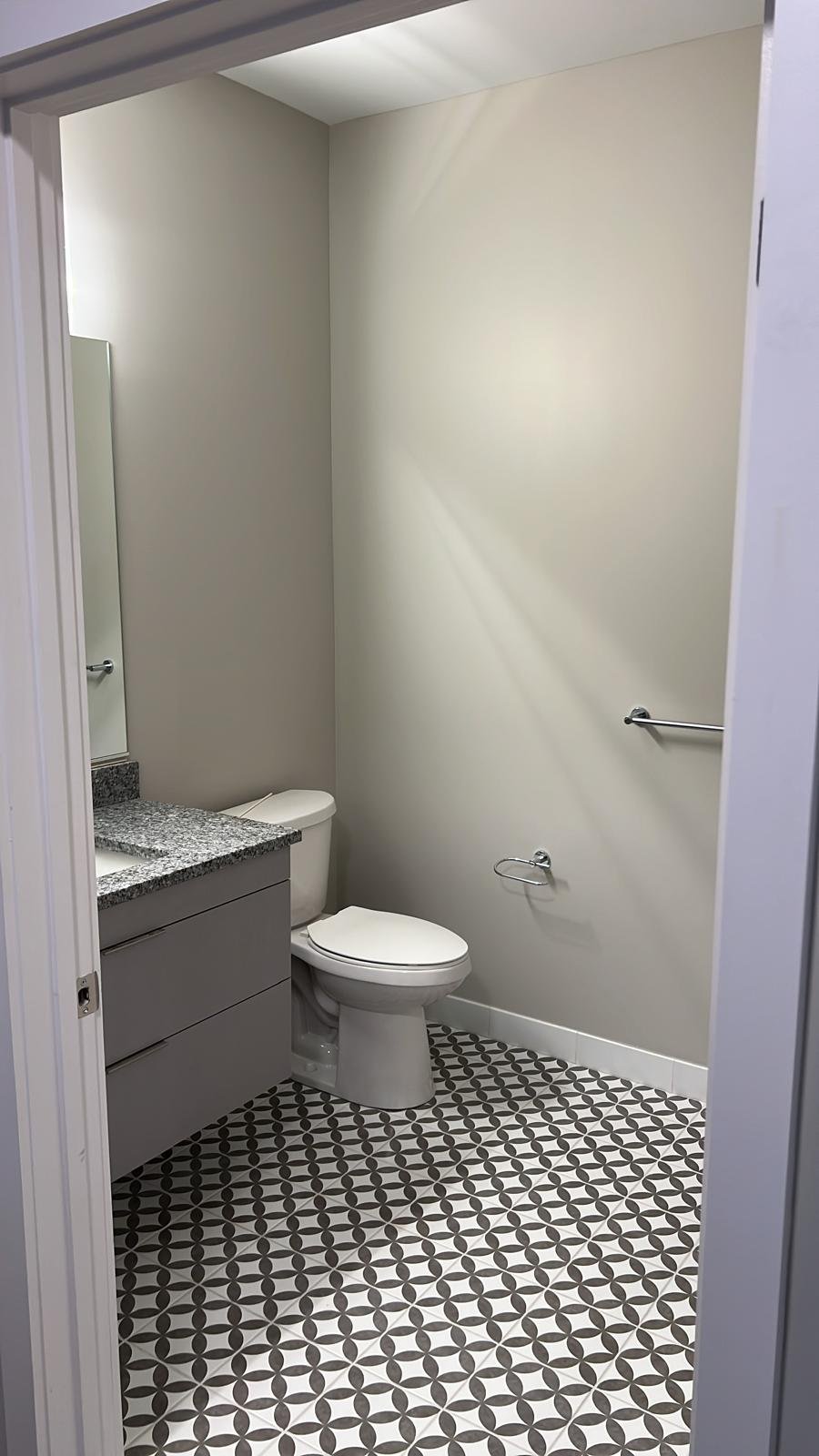 Powder room with a patterned black and white tile floor, grey vanity and granite top