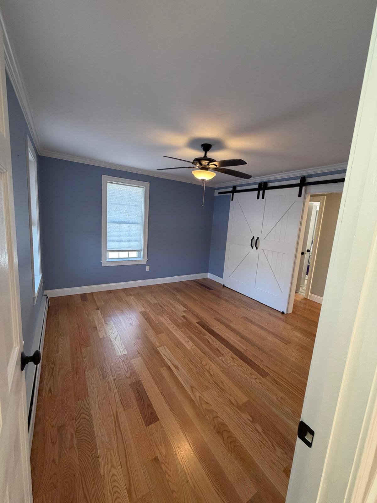 Red oak flooring in a bedroom with a barn door, crown moulding and painted walls