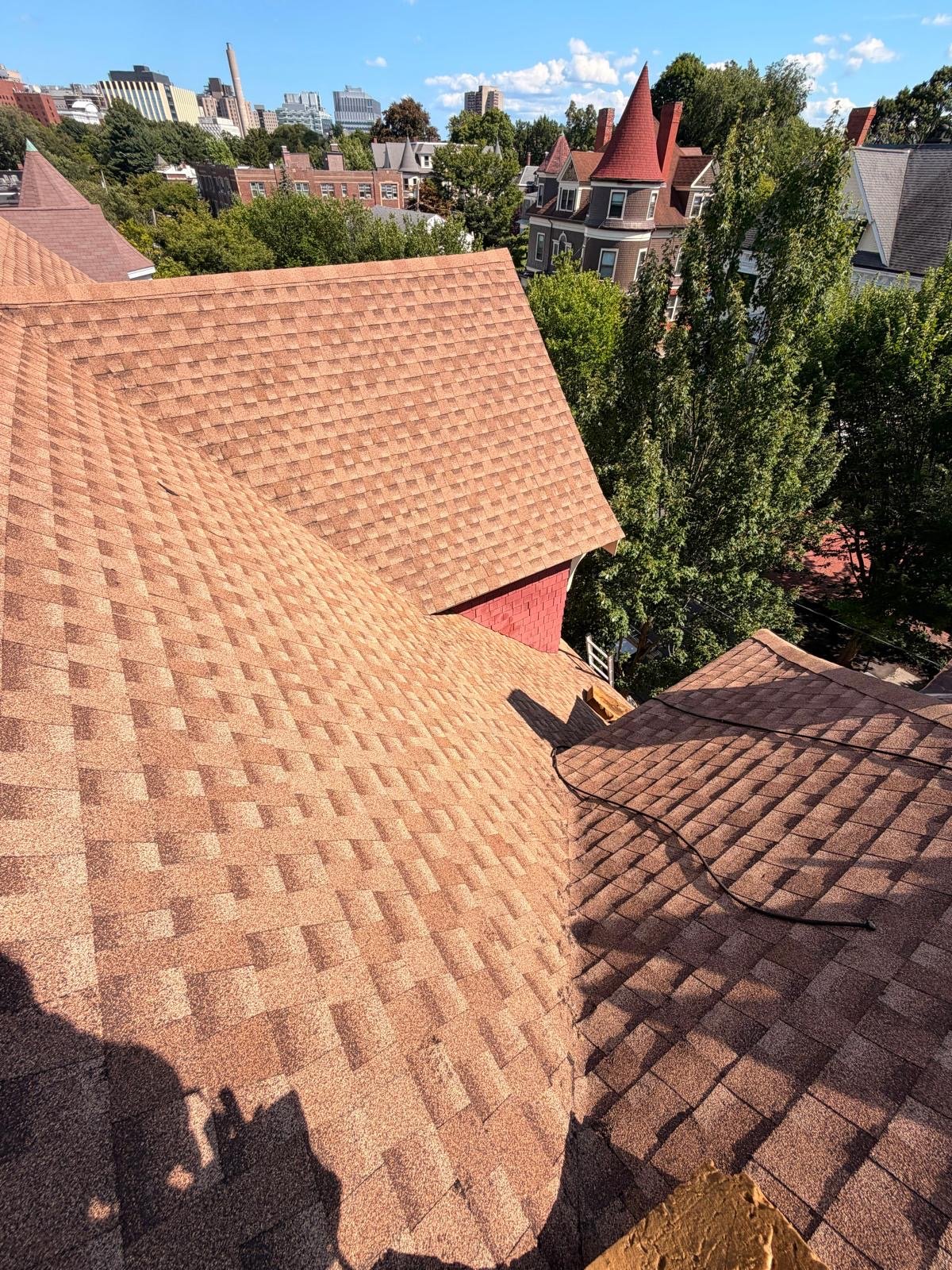 Several newly shingled roof planes meeting at a valley, with the turret roof beyond