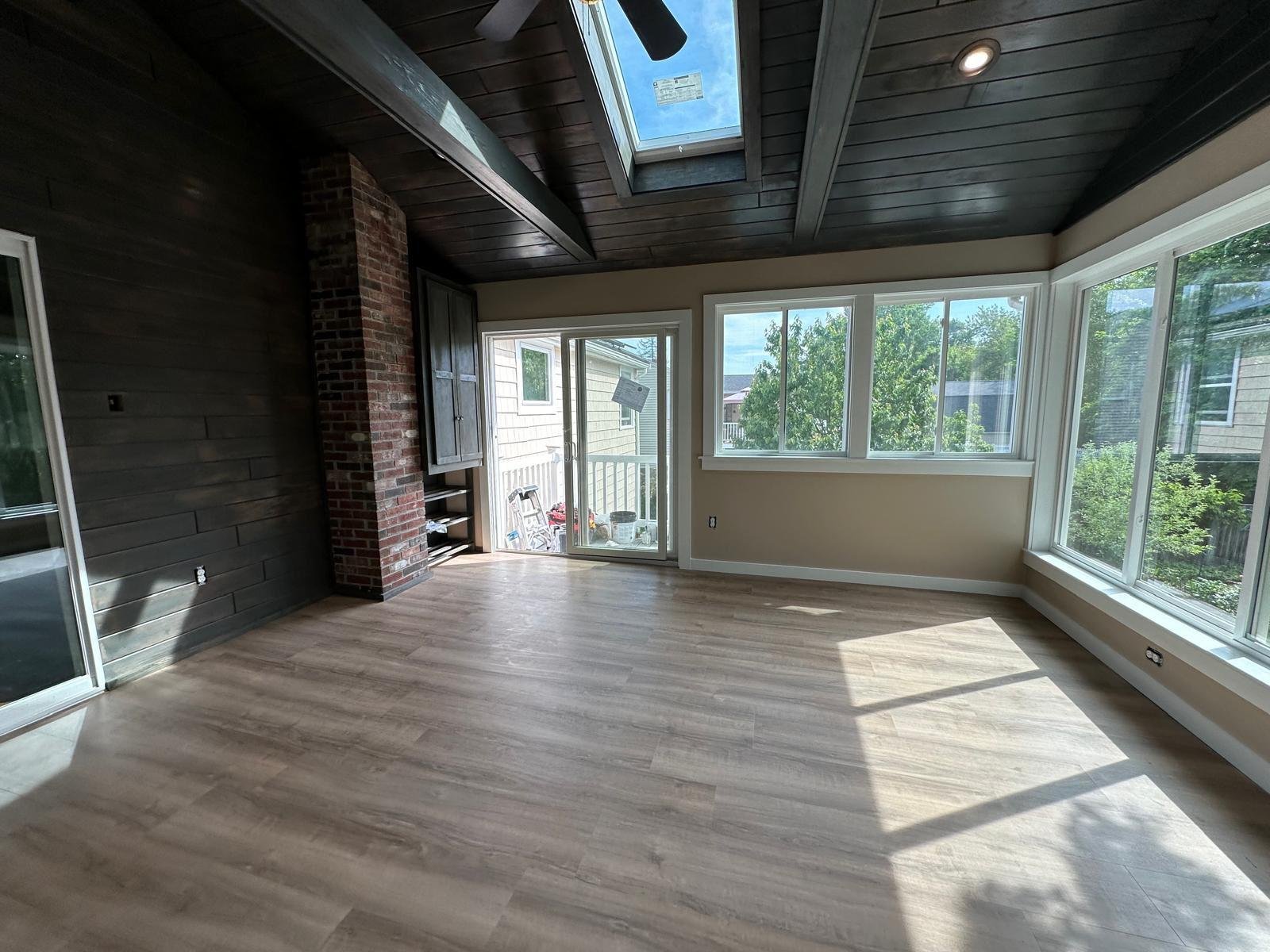 Sunroom addition with a stained shiplap wall, exposed brick chimney and new plank floor